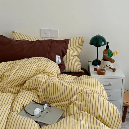 Full view of the bed with the Yellow & Brown Striped Bedding Set, showing a solid brown pillow and glasses on a laptop - RoomDen.
