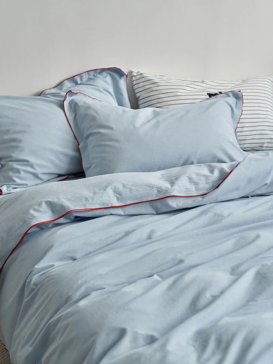 A comfortable bed dressed in a sky blue ruffle trim bedding set with a striped pillow in the background. - RoomDen