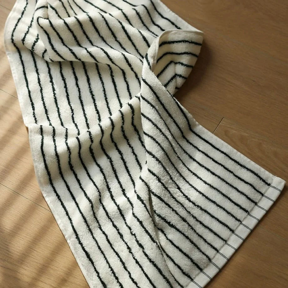 A white and black striped cotton face towel lying on a wooden surface, showing its soft terry cloth texture.