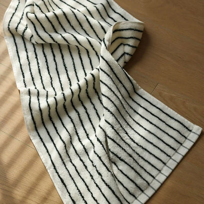 A white and black striped cotton face towel lying on a wooden surface, showing its soft terry cloth texture.