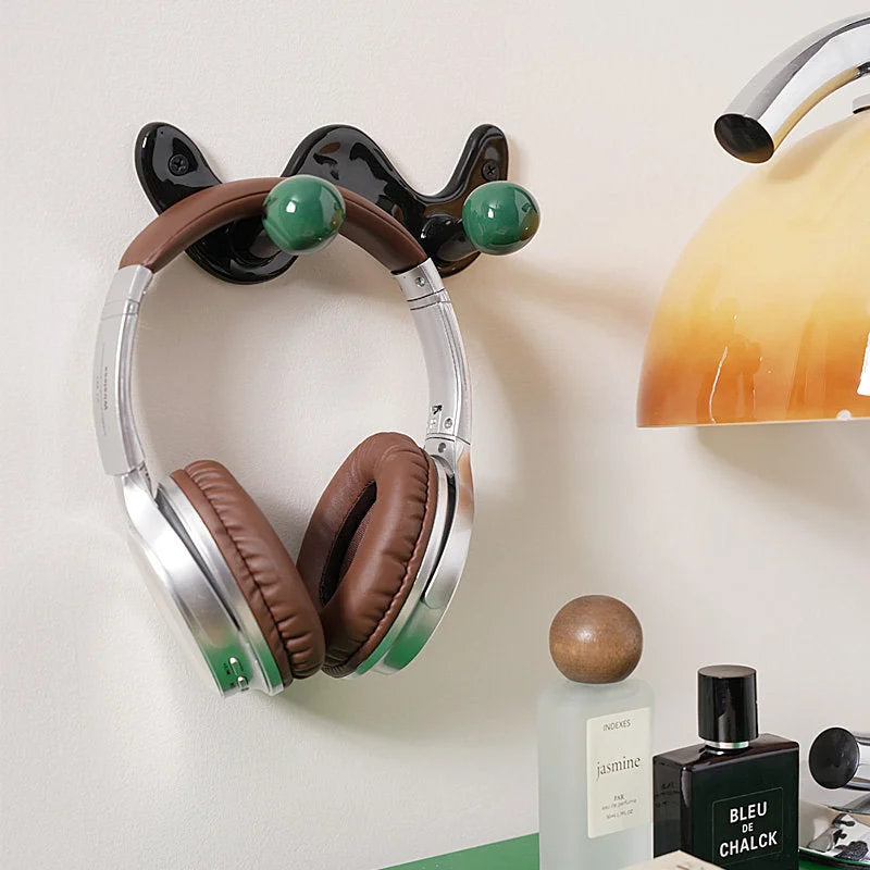 Silver headphones hanging from a black U-shaped wall hook with green balls, next to a modern lamp.