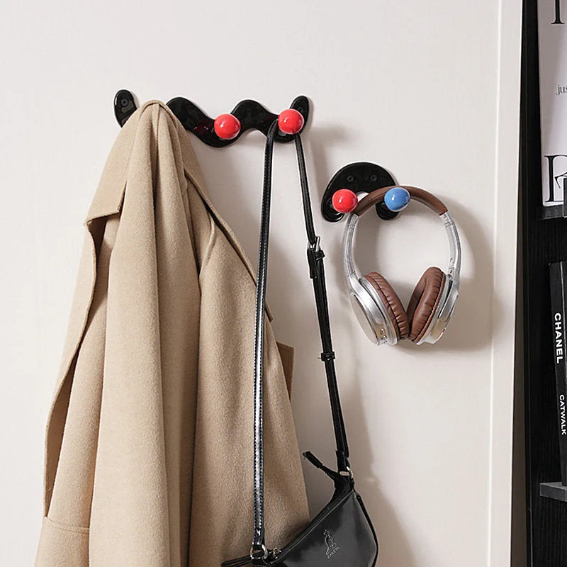 A beige coat and a black purse hanging from black wavy and U-shaped hooks with red and blue balls.