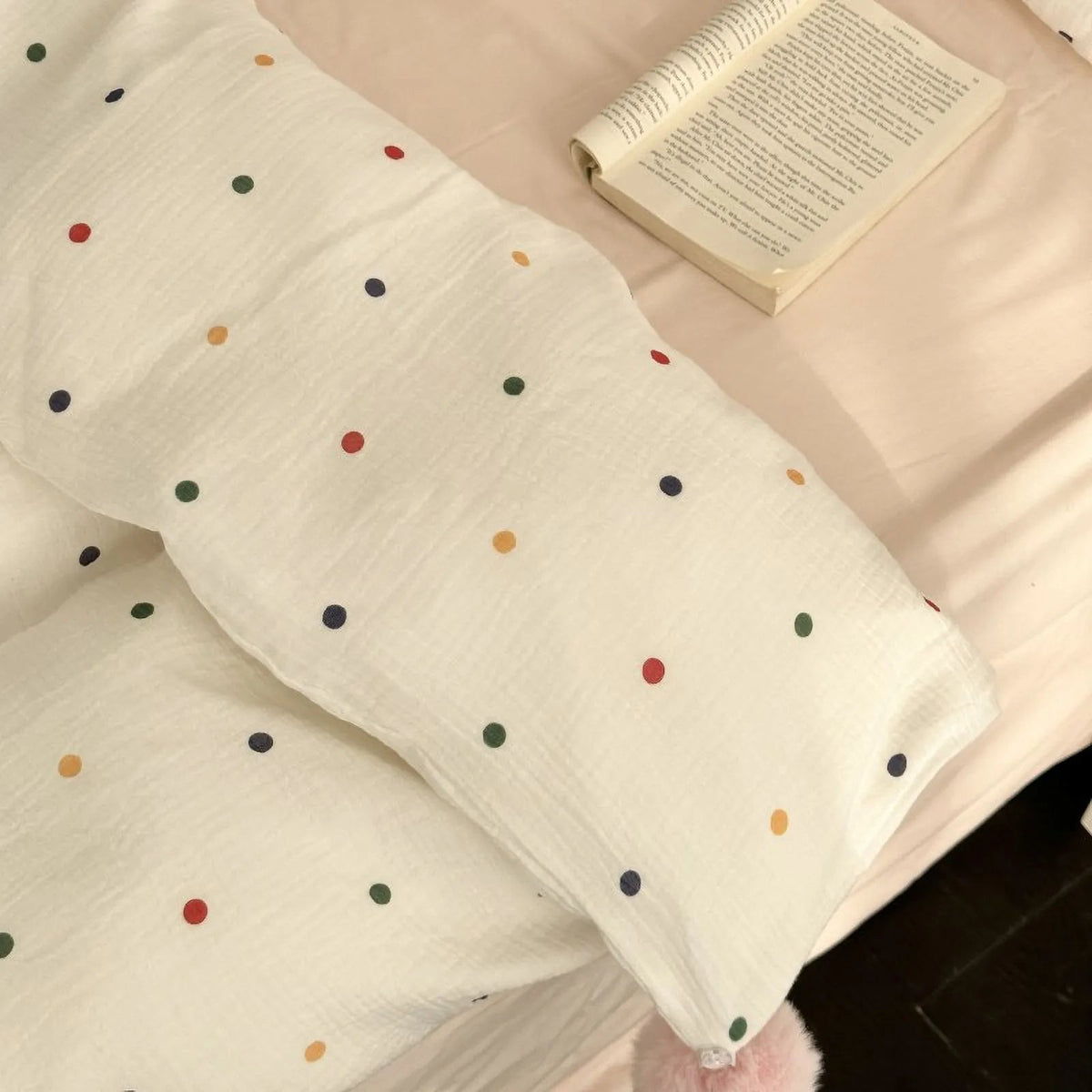 An overhead view of the soft white polka dot duvet cover with a book resting on the bed, highlighting the fabric's texture. - RoomDen