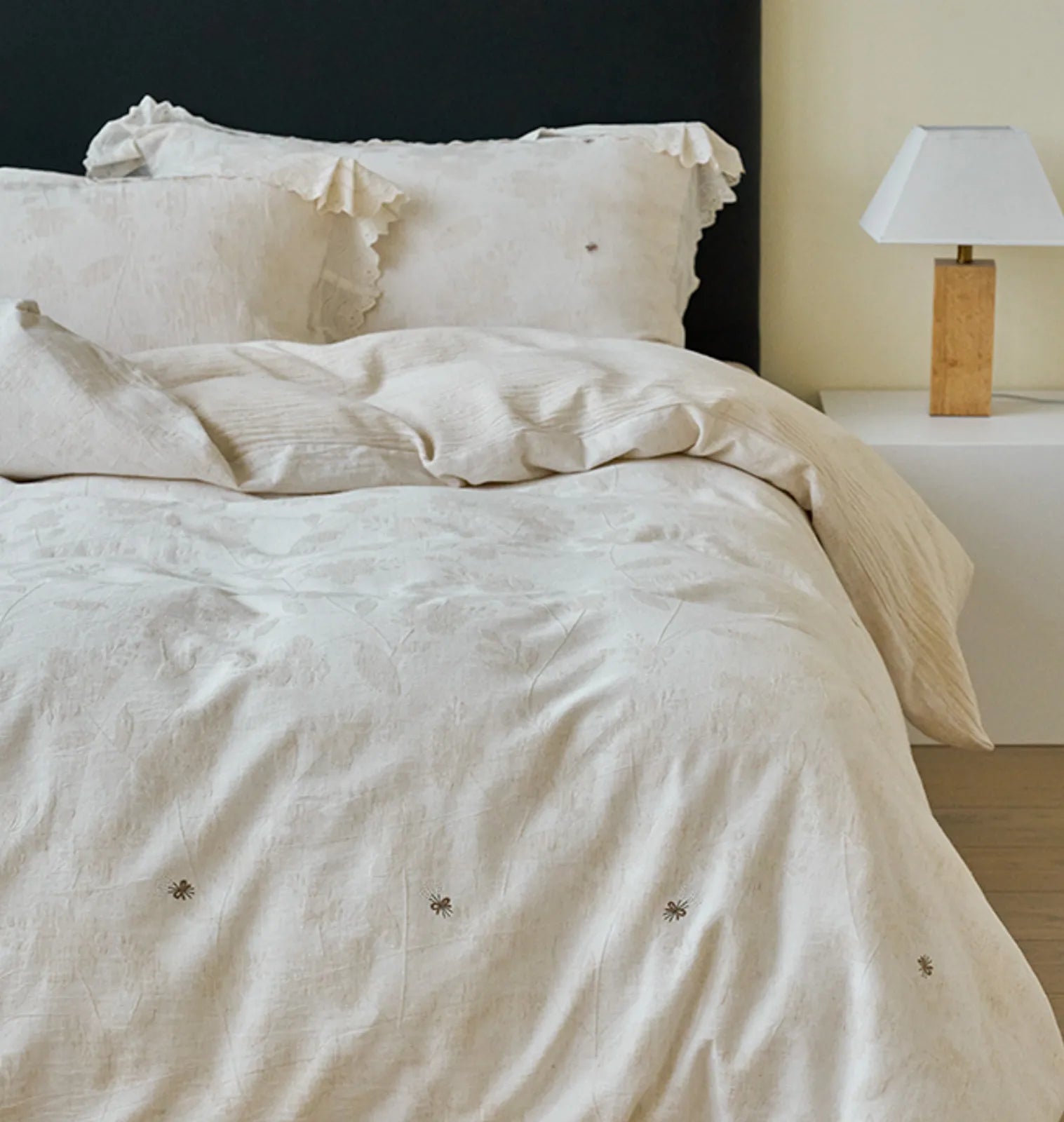 Full view of the Antique White linen duvet cover showing embroidered bee details and a bedside table - RoomDen