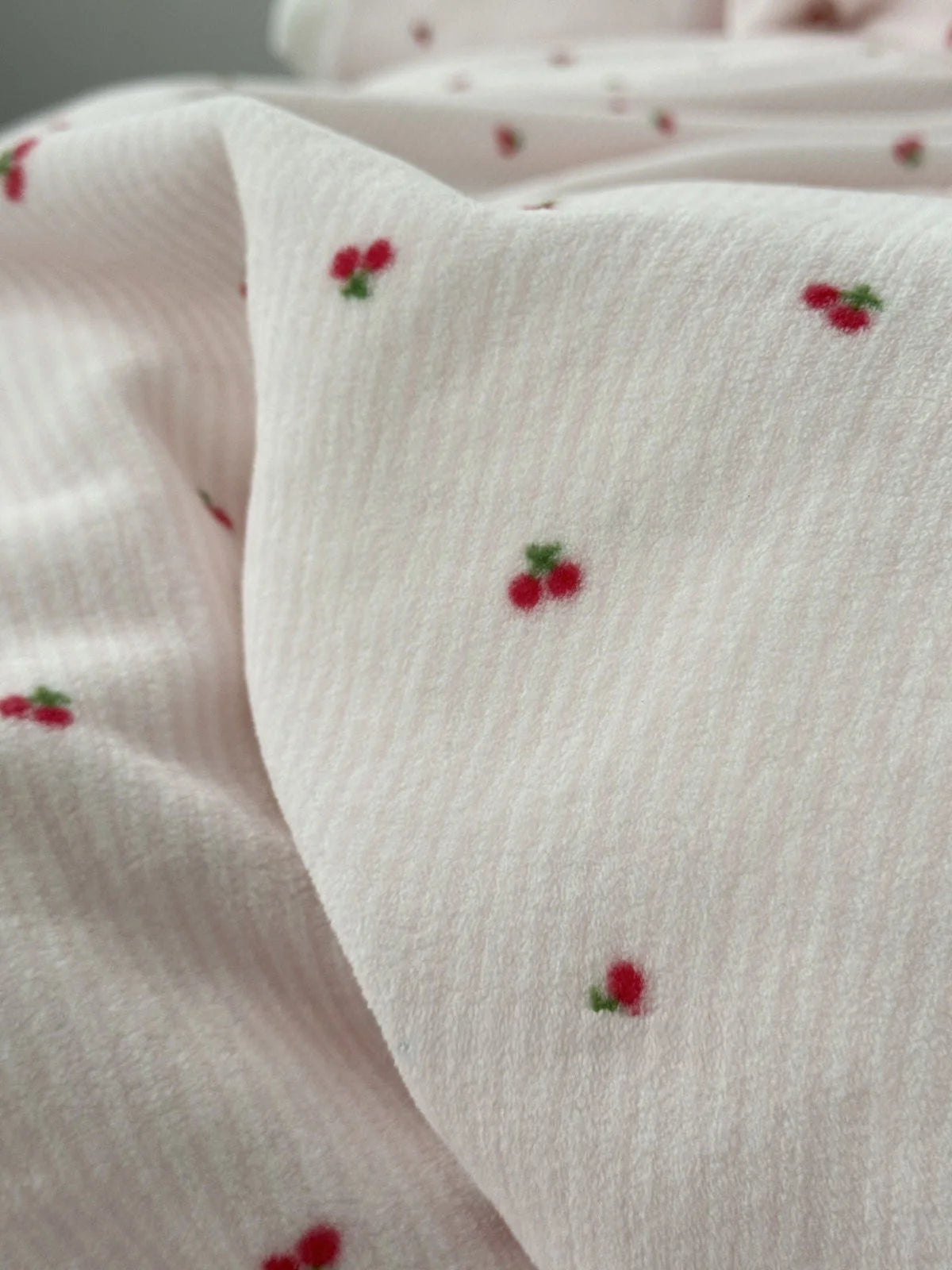 Macro shot showing the textured stripe fabric and embroidered-style cherry detail of the flannel fleece. - RoomDen