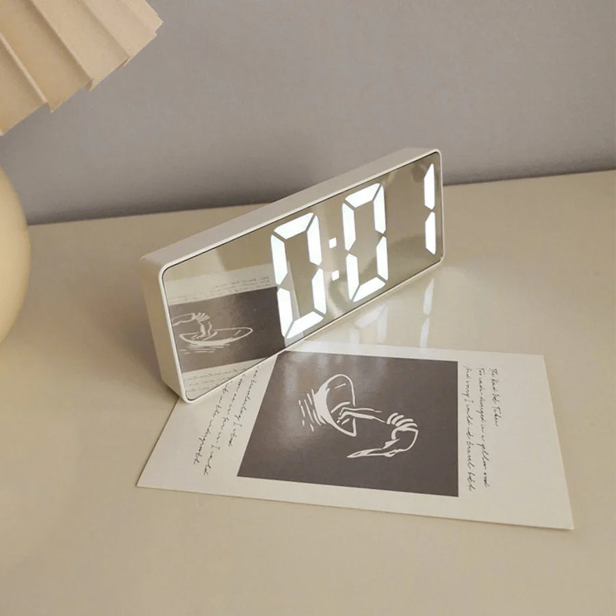 The white Sleek Mirrored Acrylic LED Table Clock showing its reflective surface on a bedside table. - RoomDen