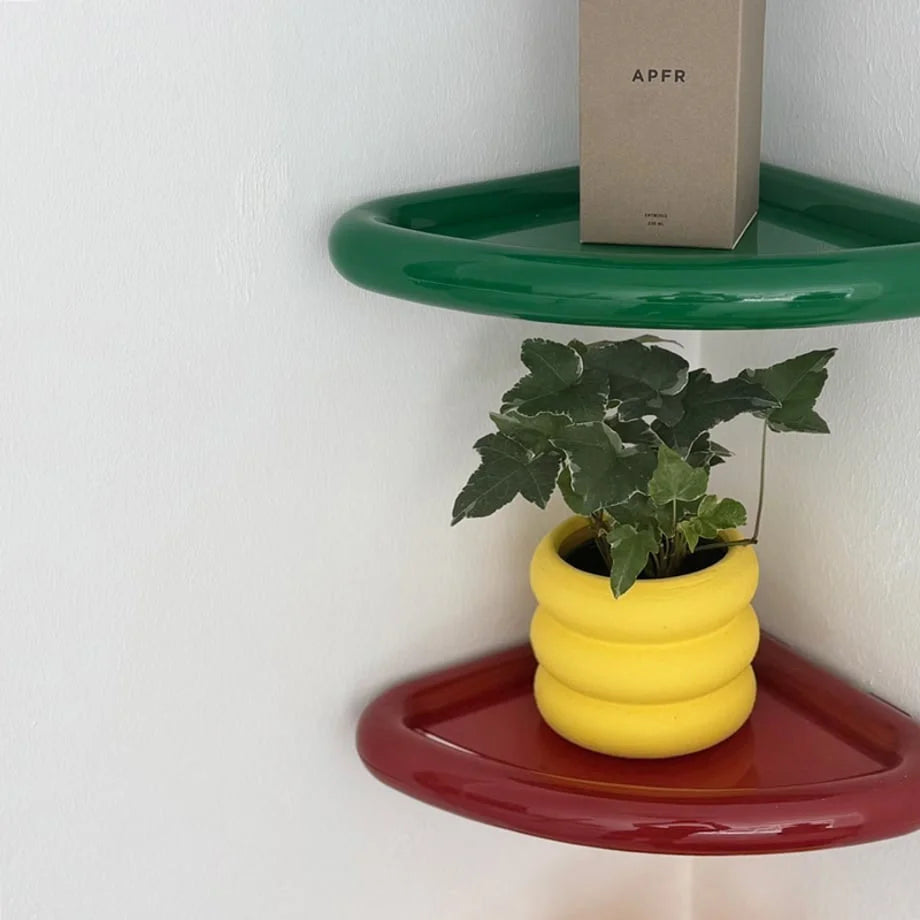 Close-up of a green and red Chunky Curved ABS Corner Shelf, holding a small plant in a vibrant yellow pot. - RoomDen