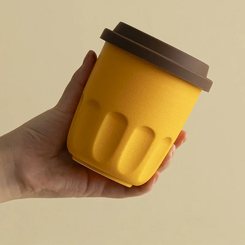 Close-up of a hand holding a mustard yellow frosted ceramic cup, showing the matte texture and grooved details. - RoomDen
