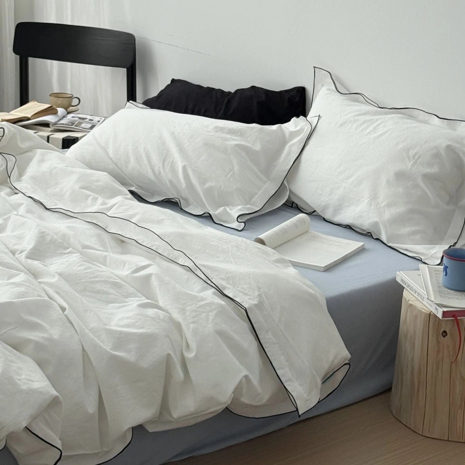 A Japandi-style bedroom with a bed made up in a white washed cotton bedding set featuring black contrast trim and ruffles. - RoomDen