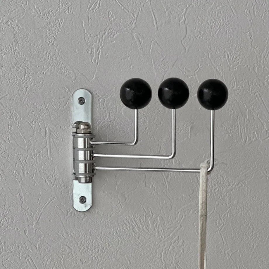Detailed shot of the black swivel wall hook's mounting plate and hinge mechanism on a grey wall - RoomDen.