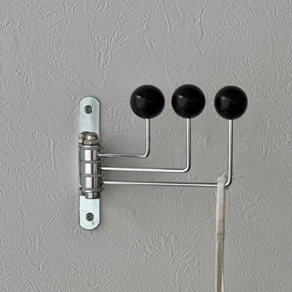 Detailed shot of the black swivel wall hook's mounting plate and hinge mechanism on a grey wall - RoomDen.