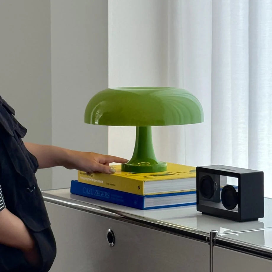 A hand touching the base of the lime green mushroom lamp, sitting on books - RoomDen.