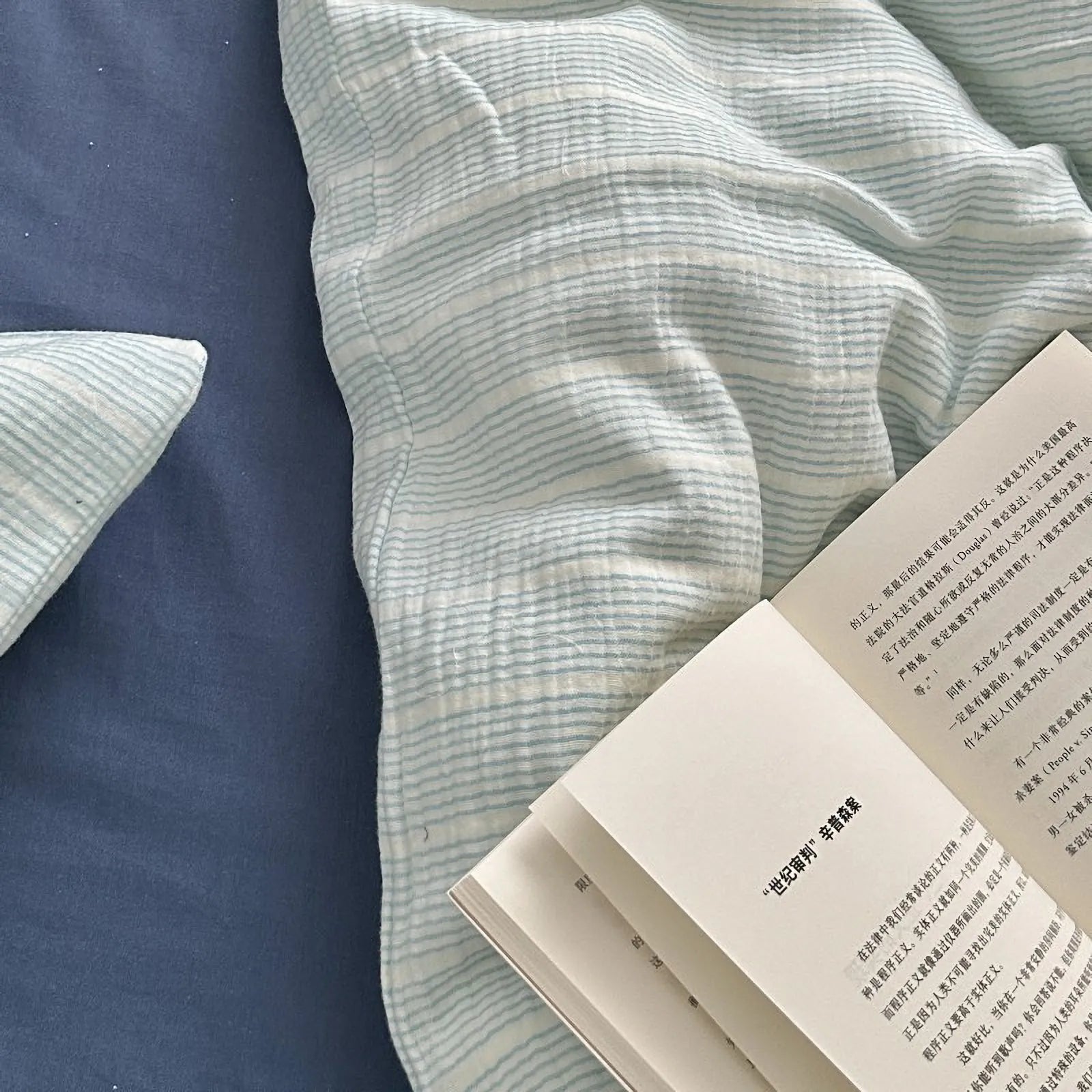 Close-up shot of the soft, crinkled texture of the cyan pinstripe washed cotton duvet cover next to an open book.