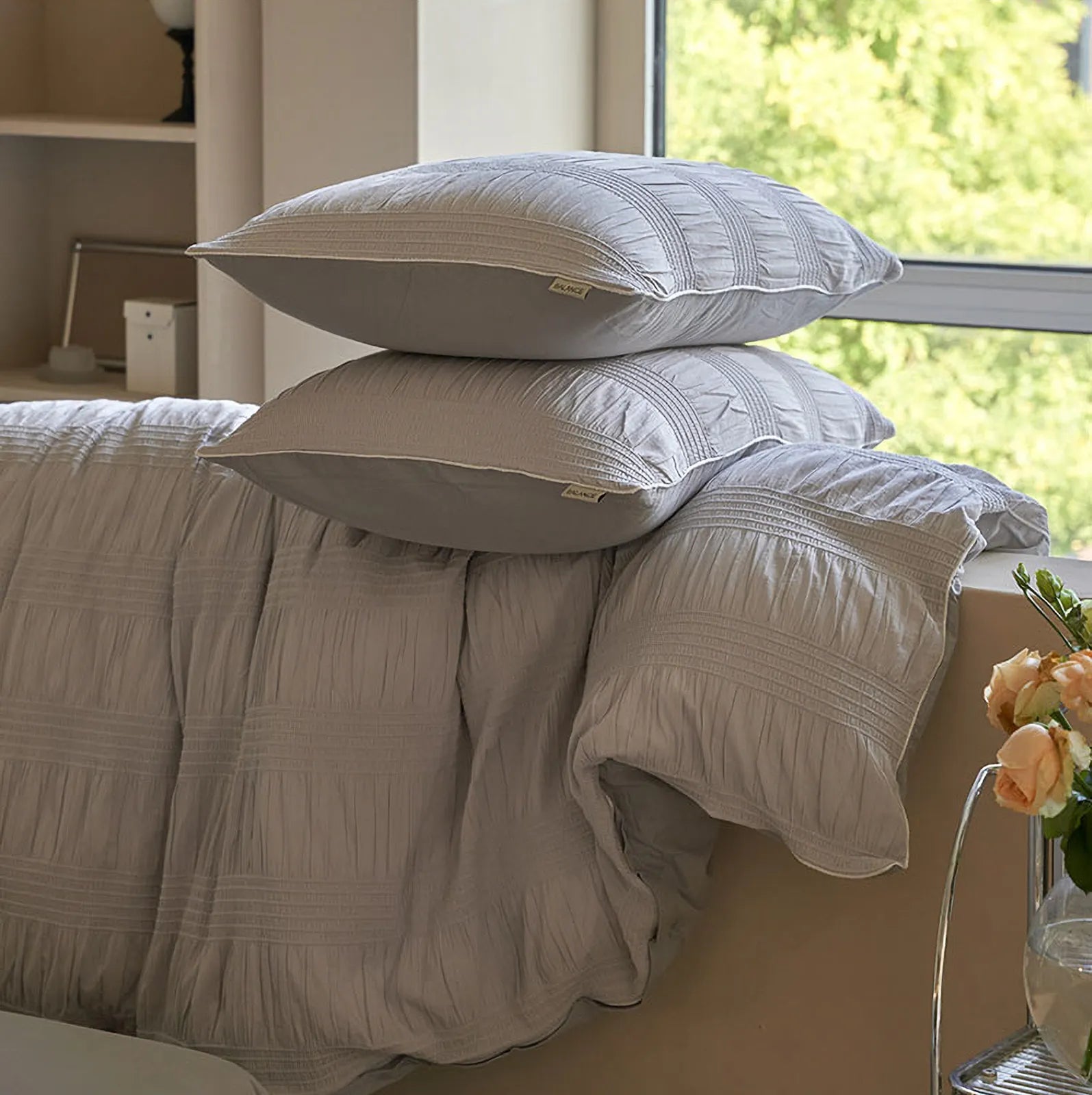 The Dove Grey pintuck duvet cover and pillows folded near a window, showcasing the texture.