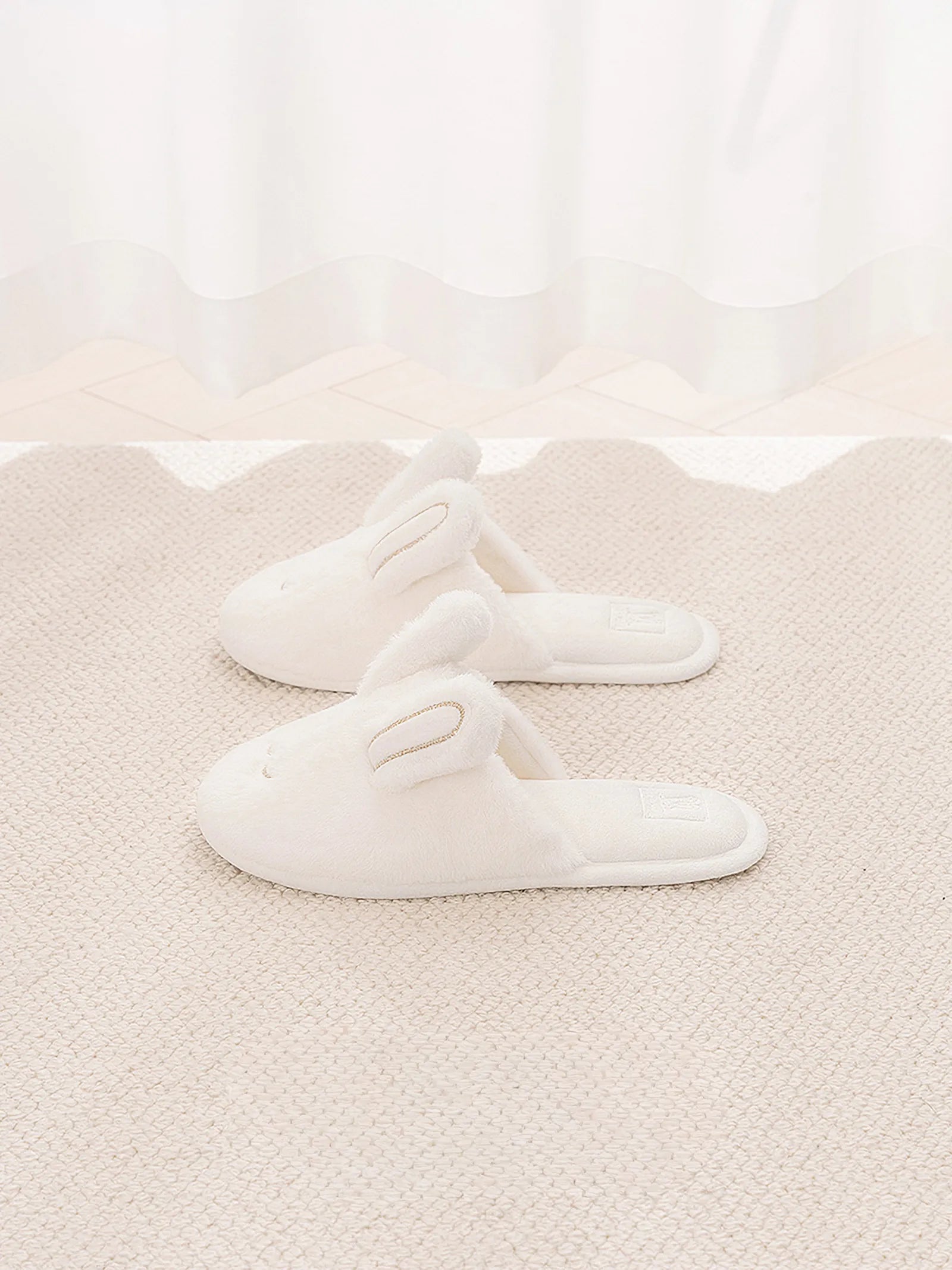 Pair of white faux fur bunny slippers on beige rug - RoomDen