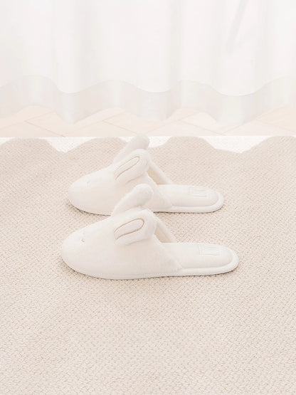 Pair of white faux fur bunny slippers on beige rug - RoomDen