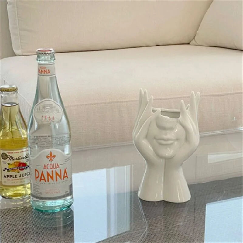 The 'Peekaboo' face vase on a glass coffee table next to drink bottles - RoomDen.