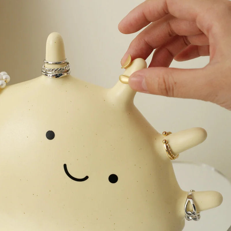 Close-up of a hand placing a ring on the Creamy Beige Matte Ceramic Smiling Sun Jewelry Organizer - RoomDen