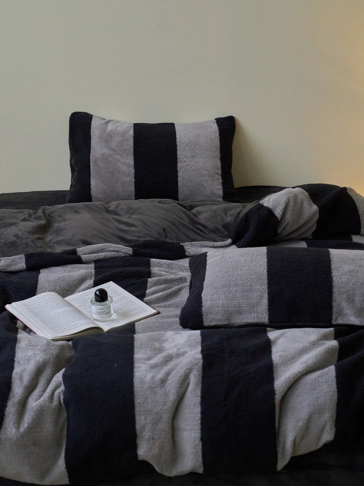 A cozy scene showing the black and grey striped fleece duvet cover and pillows, with an open book and fragrance diffuser. - RoomDen