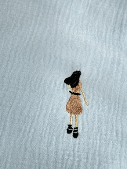 Macro shot of the sky blue washed cotton fabric, focusing on the detailed embroidery of a girl in a dress.