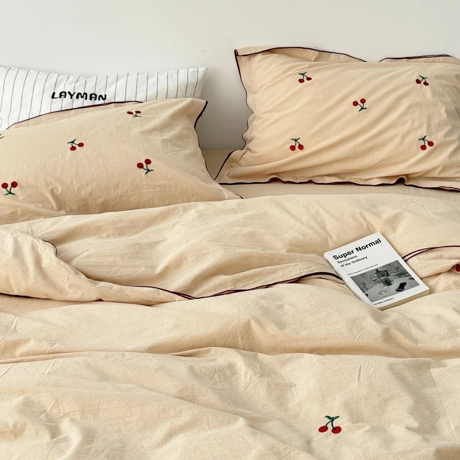 Creamy beige cherry embroidered bedding set styled with a 'Super Normal' book, showing its cozy vibe.