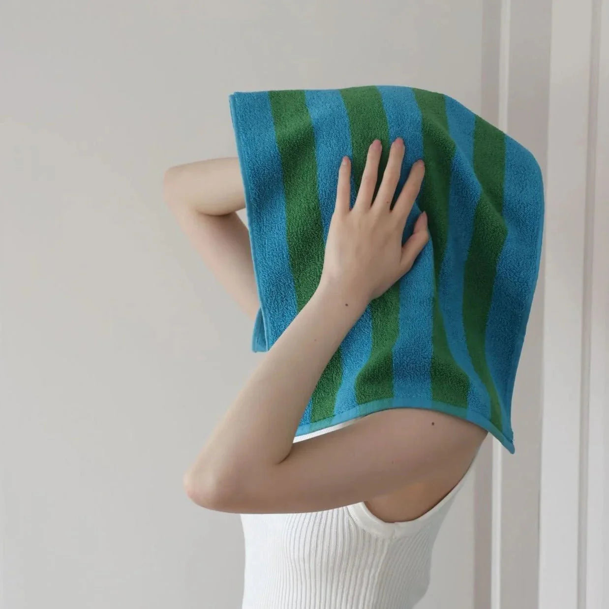 A person playfully wrapping a blue and green striped cotton face towel around their head. - RoomDen