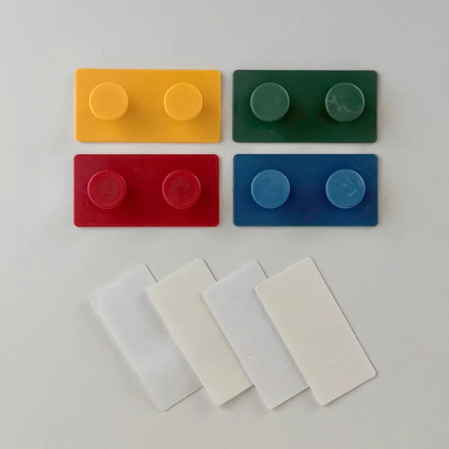 All four color variants of the Colorblock Decorative Hooks (Yellow, Green, Red, Blue) shown with their corresponding self-adhesive pads - RoomDen.