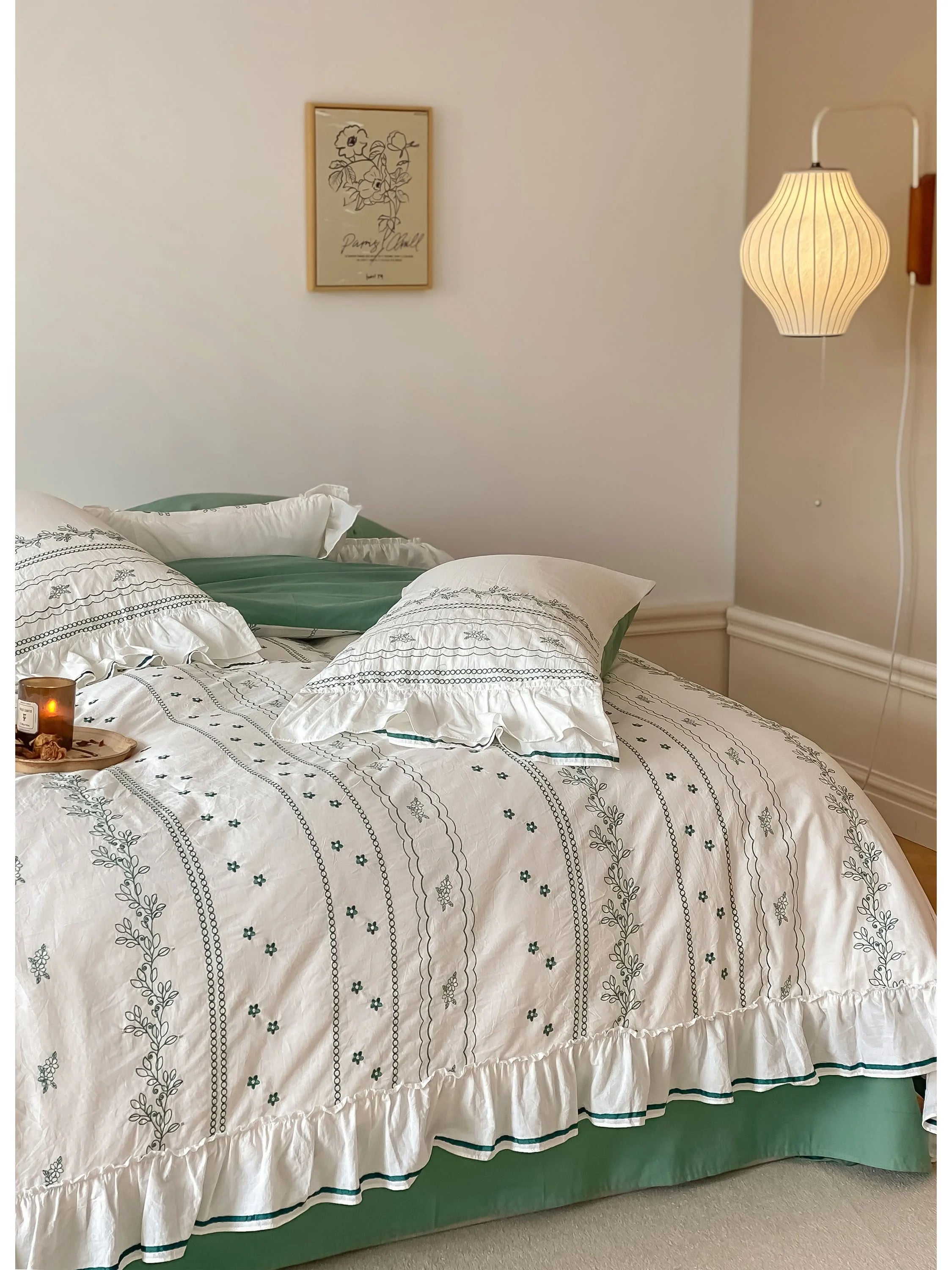 The Ruffled Floral Vine Embroidered Cotton Bedding Set in green, styled with a candle for a cozy feel.