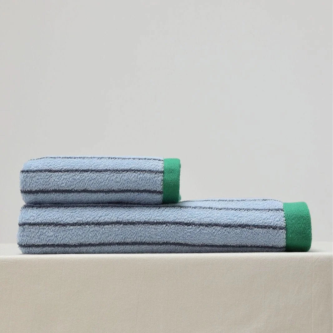 A rolled-up face towel stacked on top of a rolled-up bath towel in a blue pinstripe cotton design against a white background - RoomDen