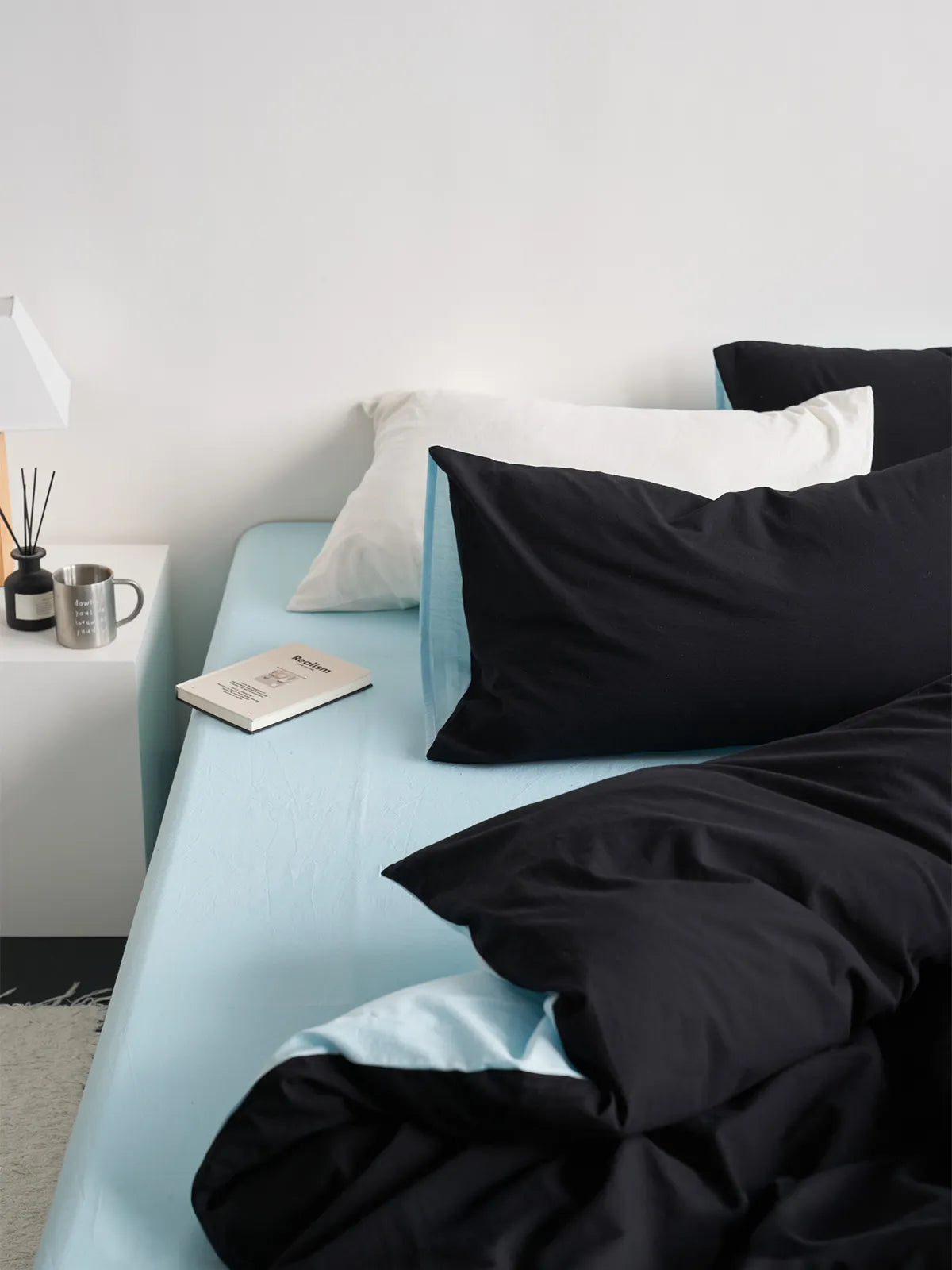 Lifestyle scene of the Reversible Two-Tone Washed Cotton Bedding Set in a bright, minimalist bedroom with a nightstand. - RoomDen