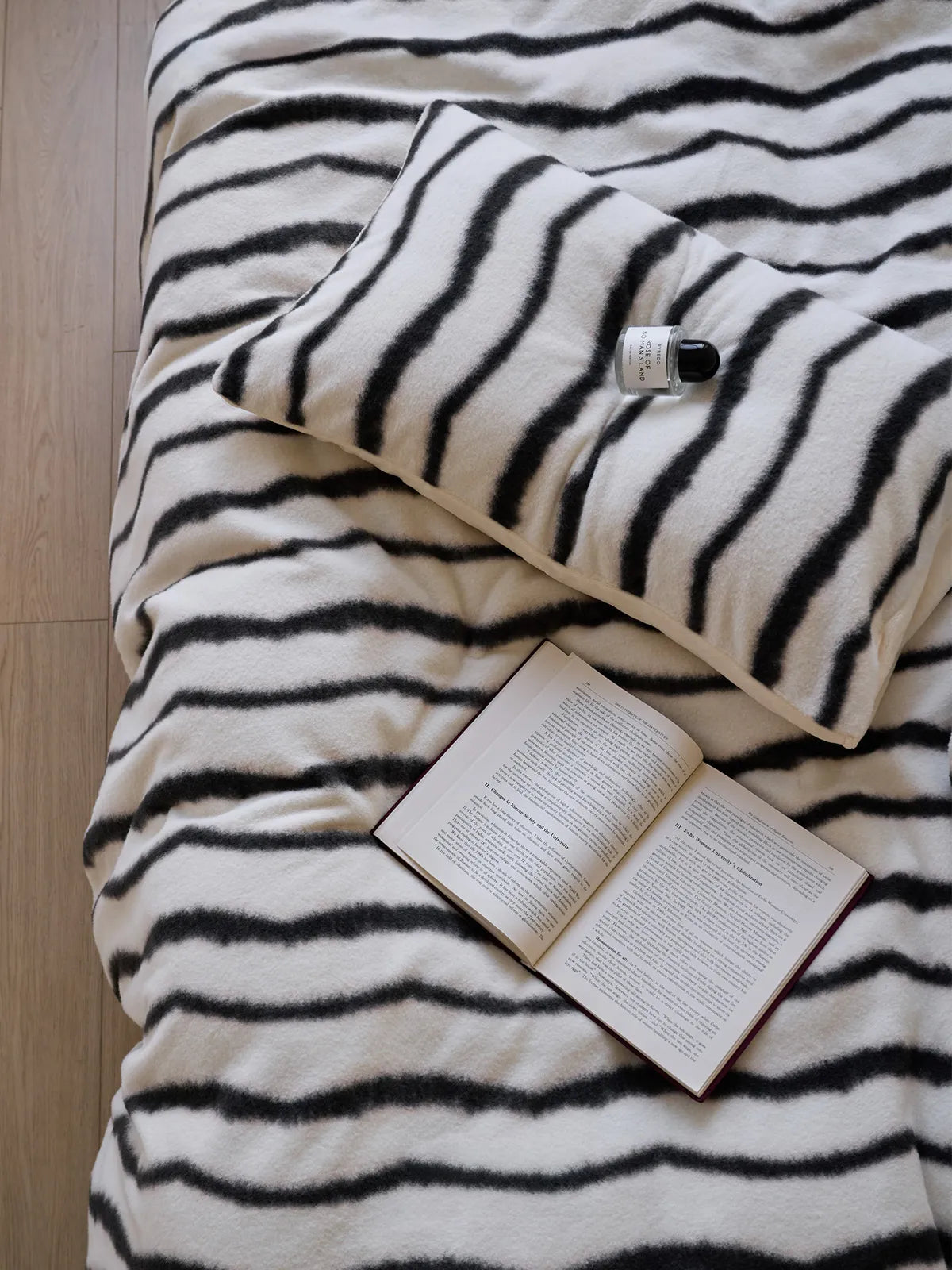 Overhead view of a black and white striped flannel fleece duvet cover with an open book and a small bottle resting on it - RoomDen.