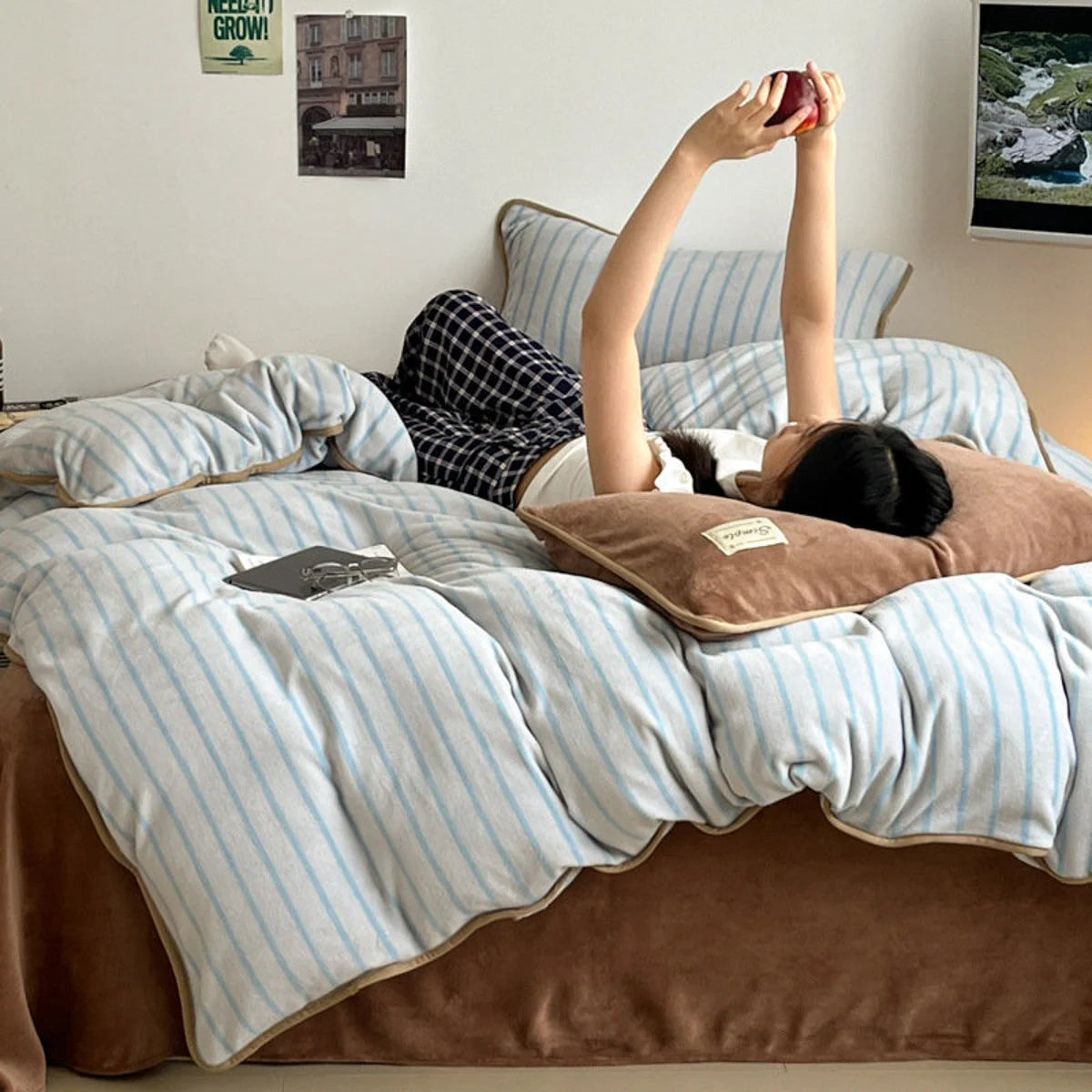 A person relaxing in the soft Mocha Brown and Blue striped flannel fleece bedding, holding an apple. - RoomDen