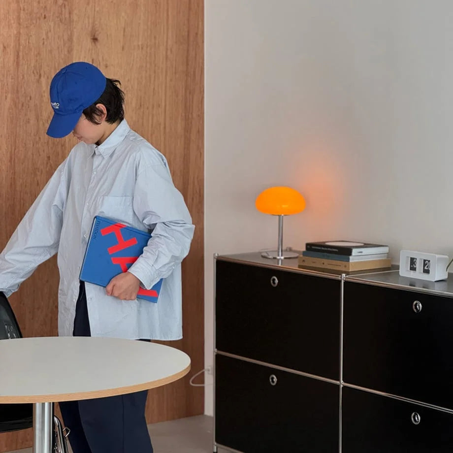 A person in a blue cap standing next to a black console table featuring the orange mushroom lamp - RoomDen.