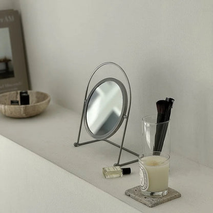 Japandi-style scene with the minimalist metal desktop mirror next to a candle and makeup brushes. - RoomDen