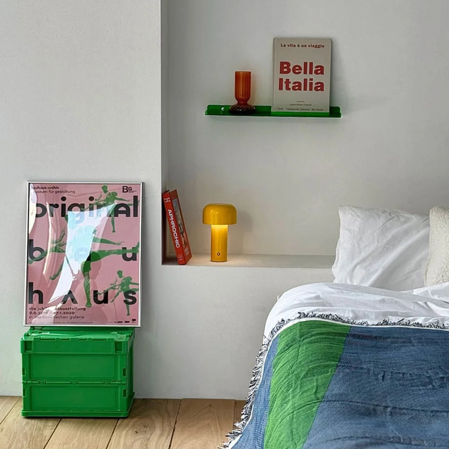 Lifestyle image of the green acrylic floating shelf installed in a cozy bedroom nook above a bed, displaying a book and vase - RoomDen.
