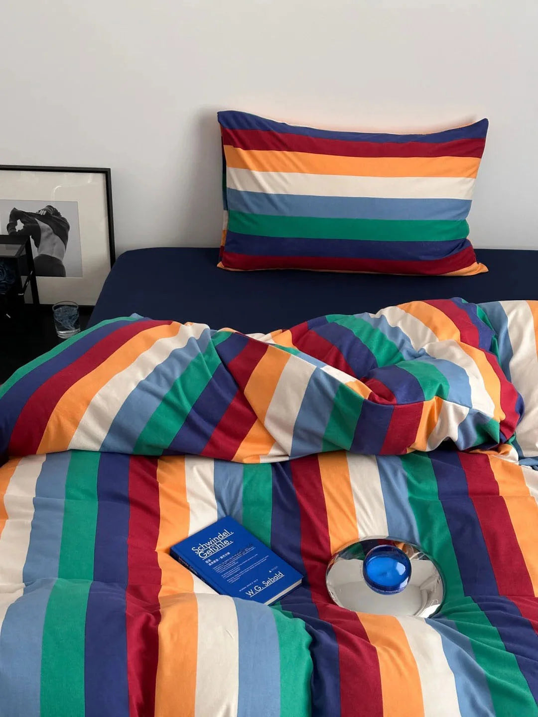 Close-up of the vibrant rainbow striped pillowcase and duvet cover, with a book resting on the bed - RoomDen