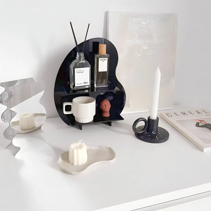 Lifestyle scene of the black wavy acrylic desktop organizer next to a candle and a book on a minimalist desk. - RoomDen