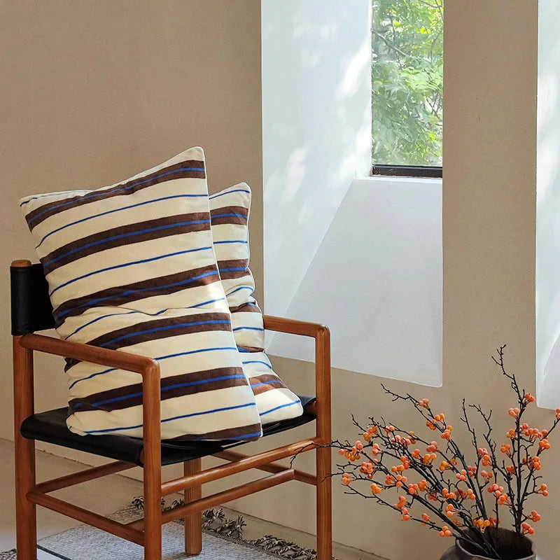 The cream and brown striped velvet pillowcases displayed on a wooden chair - RoomDen.