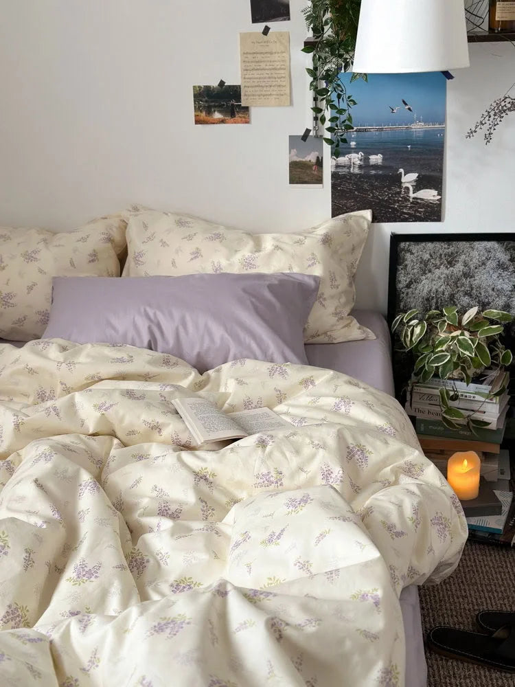 Close-up of the wisteria floral duvet cover and pillows, with an open book and candle creating a cozy atmosphere - RoomDen.