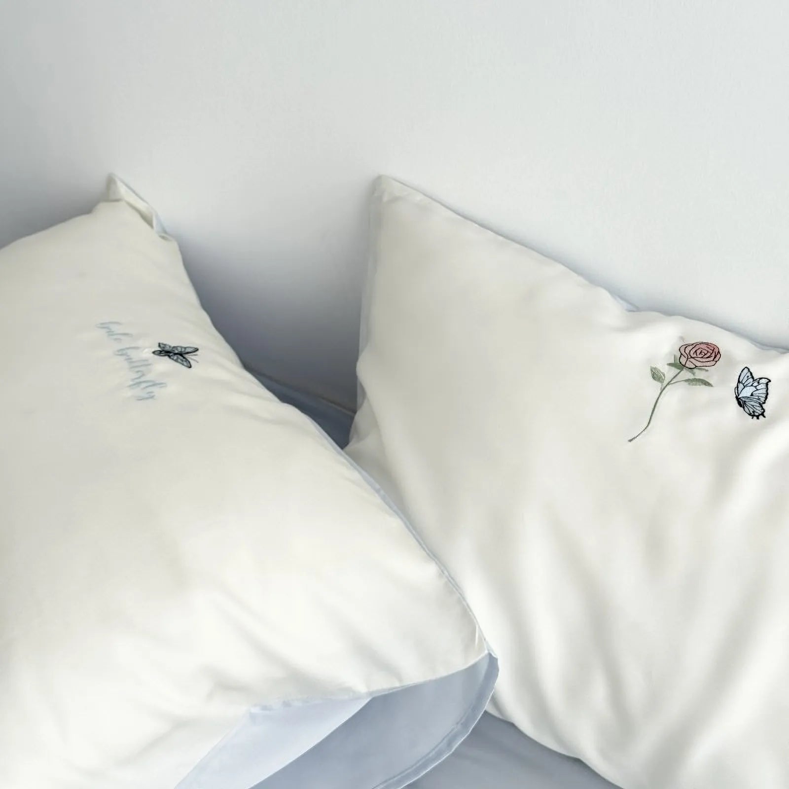 Close-up of the Cream White pillowcases, showing the contrast of the blue piping and the delicate embroidery. - RoomDen