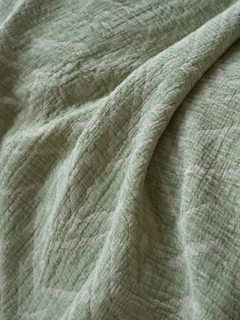 Close-up of the soft crinkled texture and subtle geometric pattern on the sage green washed cotton, showing how the raised face hides a hard wrinkle. — RoomDen