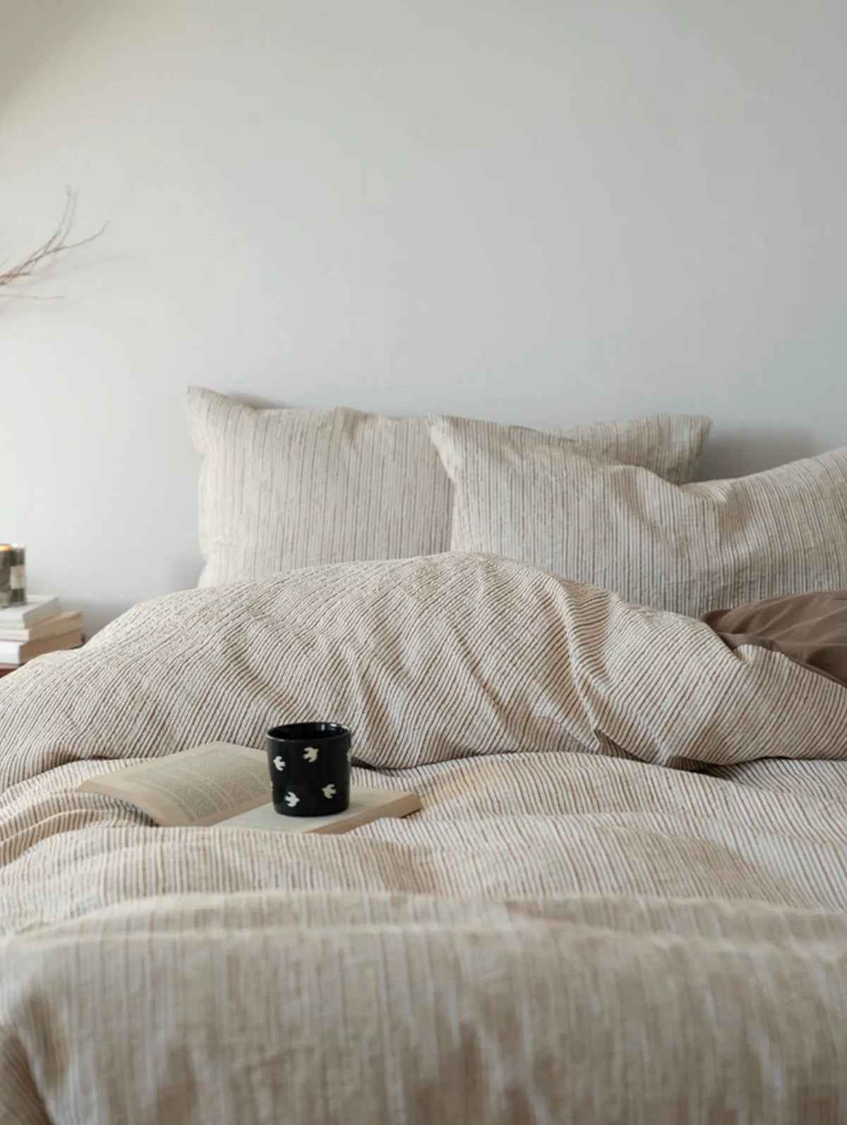 Cozy bed scene featuring the Latte Brown pinstripe bedding with a book and coffee mug - RoomDen