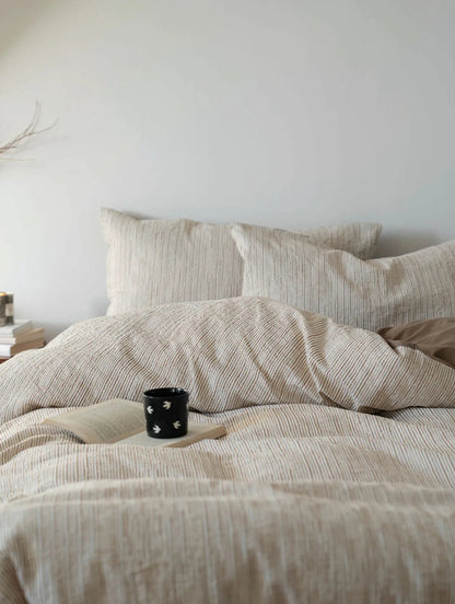 Cozy bed scene featuring the Latte Brown pinstripe bedding with a book and coffee mug - RoomDen