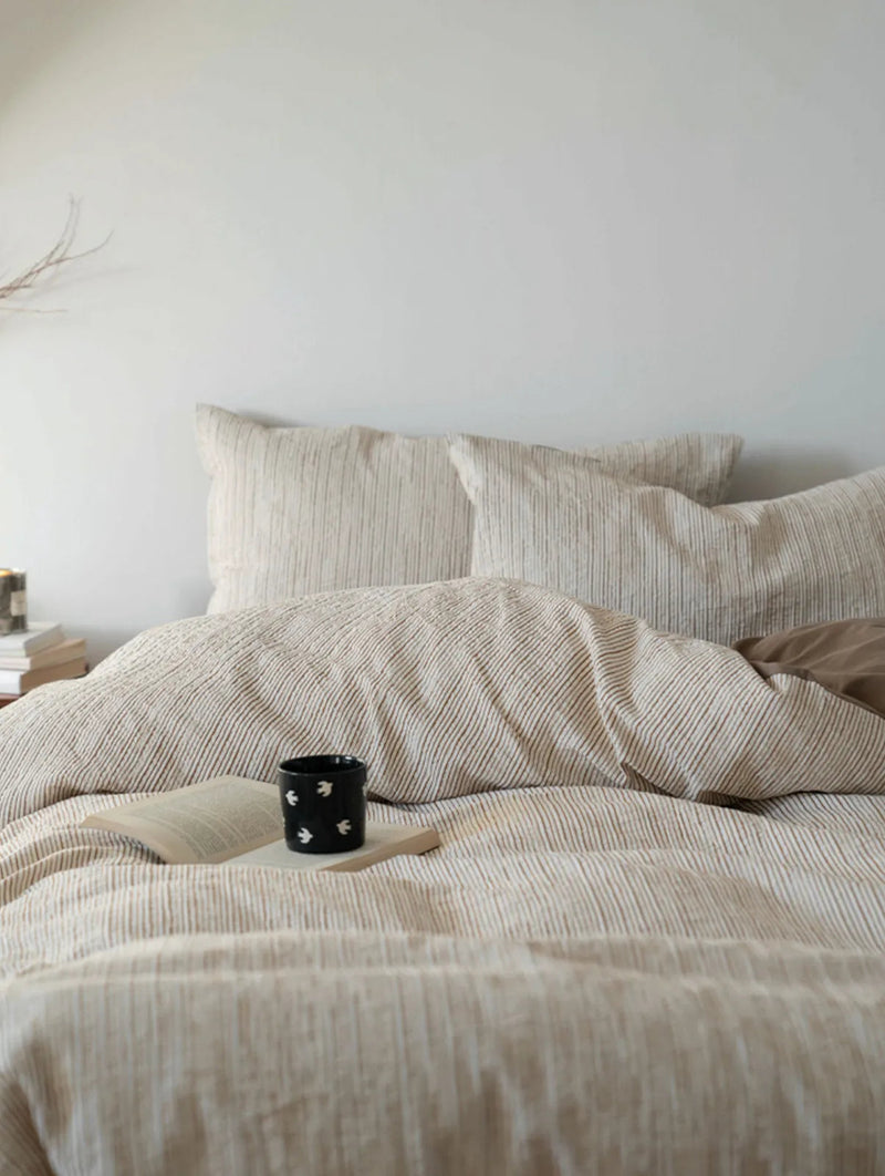 Cozy bed scene with the Latte Brown pinstripe bedding, a book and a coffee mug on the duvet. — RoomDen