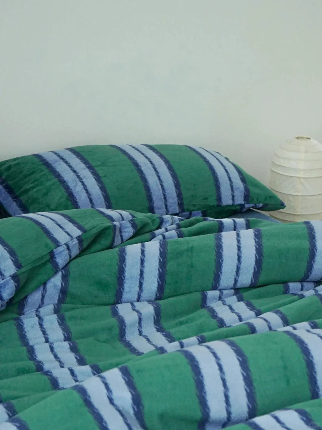 Emerald green and blue striped velvet pillowcases and duvet cover on a bed - RoomDen.