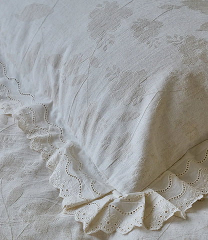 Close up of creamy linen pillowcase with floral embroidery and eyelet lace ruffle detail RoomDen.