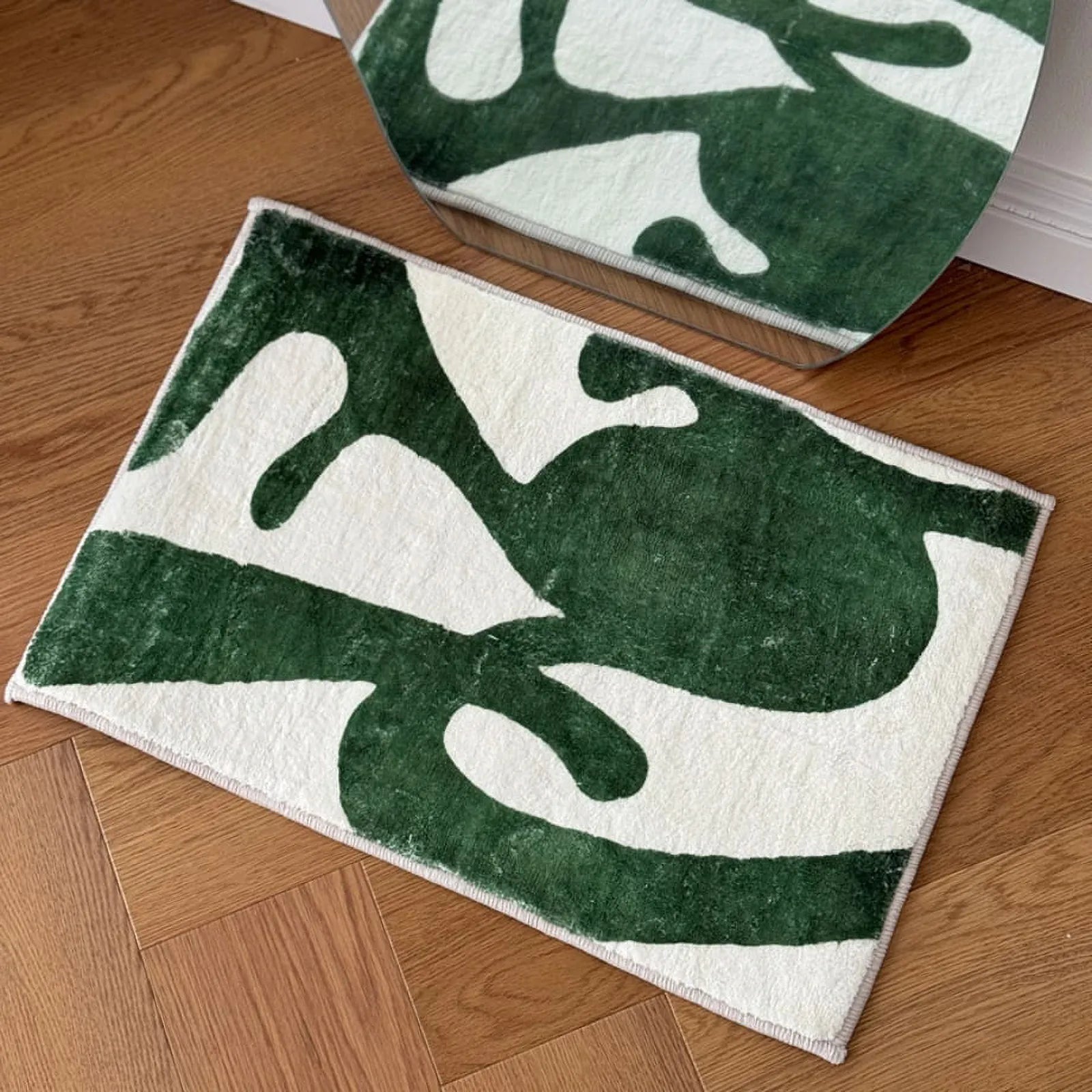 Top-down view of RoomDen Matisse style green and white abstract art rug on a wooden floor.