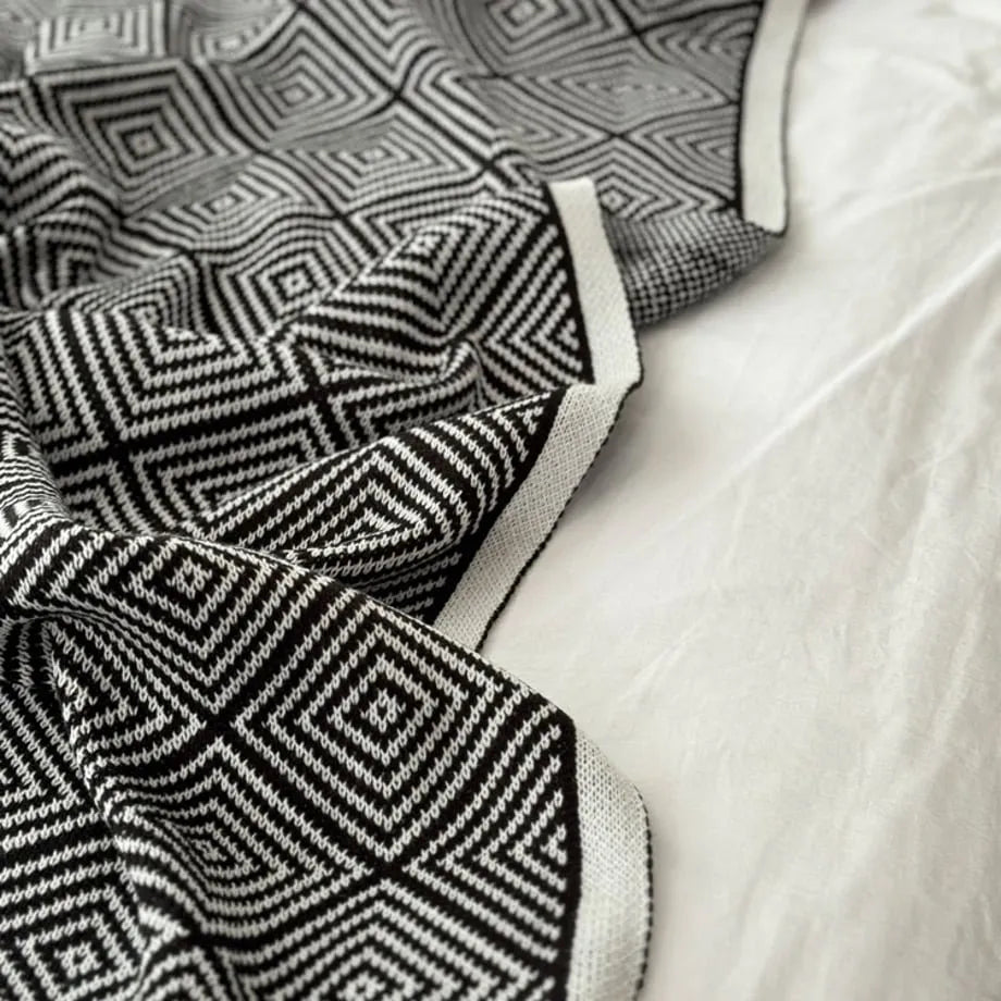 Black and white diamond knit fleece throw blanket draped over a wooden chair - RoomDen