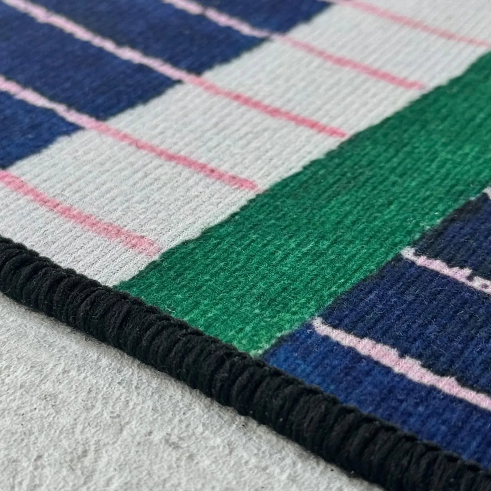 Close-up texture shot showing the blue and green tufted pile and subtle pink stitching details of the RoomDen rug.