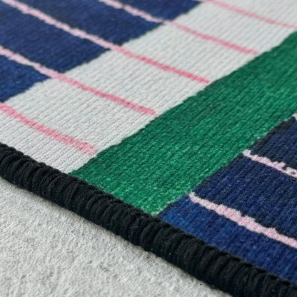 Close-up texture shot showing the blue and green tufted pile and subtle pink stitching details of the RoomDen rug.